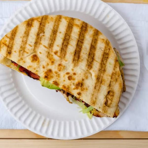 Grilled quesadilla with meat, lettuce, and avocado on a white paper plate.