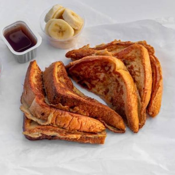 Golden brown French toast slices with a side of syrup and banana slices on white paper.