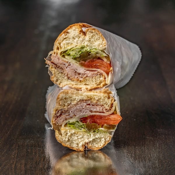 A Bodega Bros deli sandwich, cut in half, revealing turkey, cheese, lettuce, tomatoes, and pickles.
