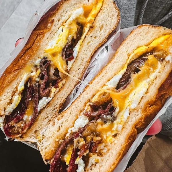 A Bodega Bros deli sandwich, cut in half, revealing steak, eggs, and melted cheese.
