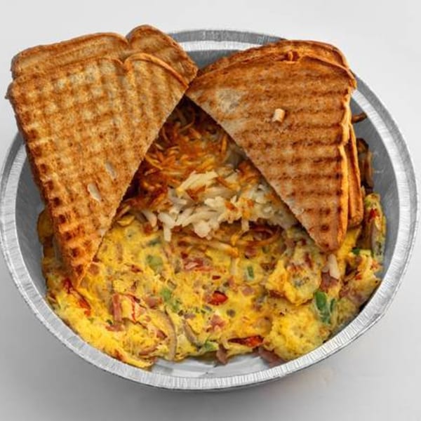 A deli breakfast platter with scrambled eggs, hash browns, and two pieces of toast in a foil container.