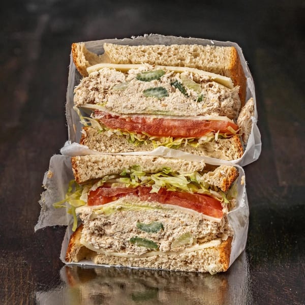 Two halves of a Bodega Bros deli sandwich with chicken salad, lettuce, tomato, and cheese.