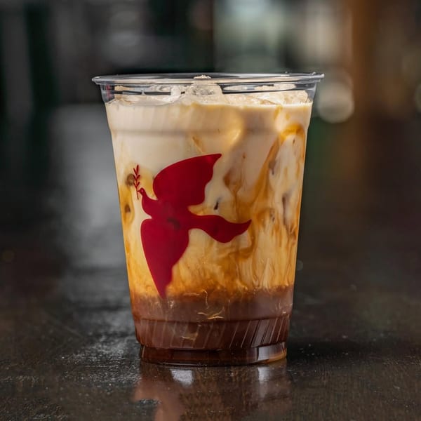 Iced coffee with milk and caramel swirls in a clear plastic cup with a red Bodega Bros logo.