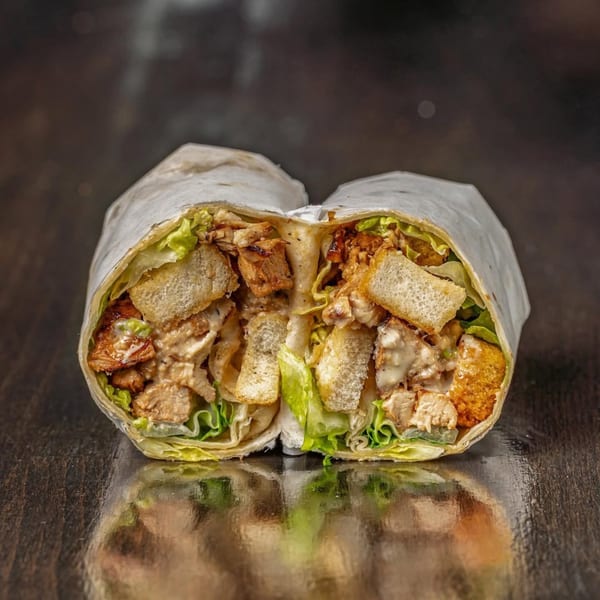 A Bodega Bros deli wrap, cut in half, revealing chicken, croutons, lettuce, and sauce.